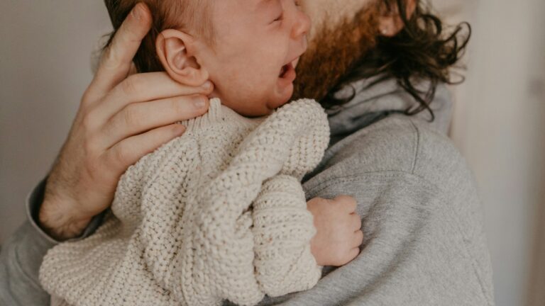 Um bebe chora inconsolavelmente no colo do pai.