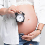 Uma mulher grávida segura um relógio na sua barriga