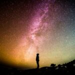 Um homem olhando para a Via Lactea com cores laranja e roxa vibrantes