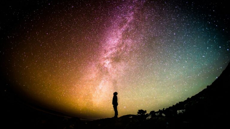 Um homem olhando para a Via Lactea com cores laranja e roxa vibrantes